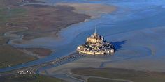 an island in the middle of water surrounded by sand and other landforms with buildings on it