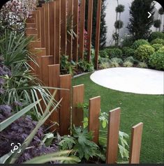 a wooden fence in the middle of a lush green yard with purple flowers and greenery