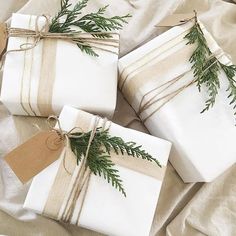 three wrapped presents are tied with twine and decorated with greenery, on top of a bed