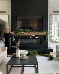 a woman standing in front of a fireplace with christmas garland on it's mantle