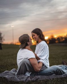 a man and woman sitting on top of a blanket in the middle of a field