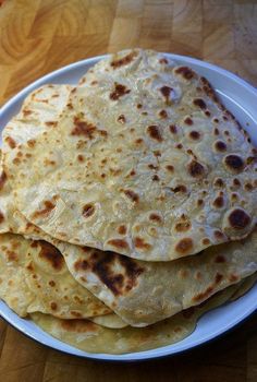 three flat breads on a white plate sitting on a wooden table