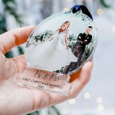 a hand holding a glass ornament with a photo of a bride and groom on it