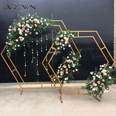 two metal stands with flowers and greenery on them in front of a black wall