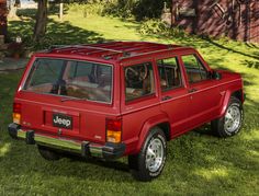 a red jeep parked on top of a lush green field