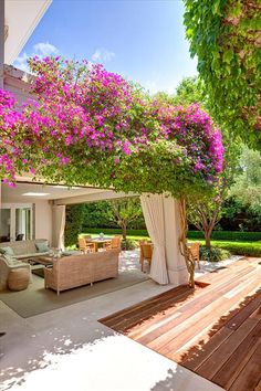 an outdoor living area with wooden decking and purple flowers growing on the trees overhang