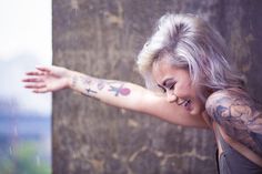 a woman with white hair and tattoos on her arm reaching out to touch the wall