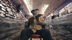 a man sitting on top of a red chair in a room filled with shelves full of cds