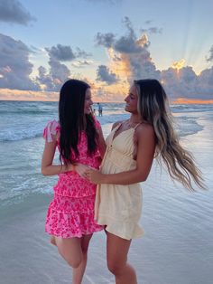 two young women standing on the beach with their arms around each other as they talk