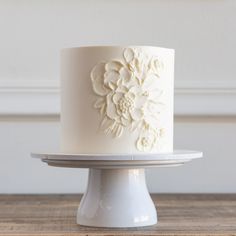 a white wedding cake with flowers on the top is sitting on a plate in front of a wall