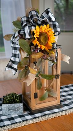 a wooden lantern with a sunflower in it on top of a checkered table cloth