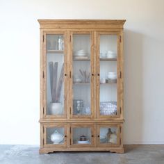 a wooden china cabinet with glass doors on the top and bottom shelves, in front of a white wall