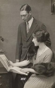 an old black and white photo of a man and woman looking at something on a desk