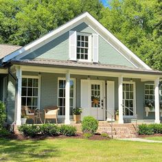 a blue house with white trim and windows on the front porch is surrounded by greenery