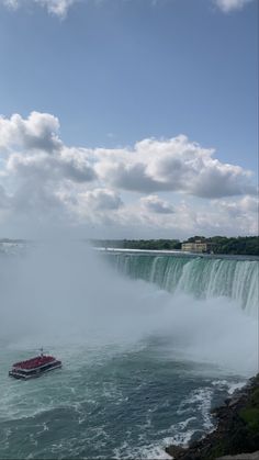 a boat is in the water near a large waterfall and clouds are flying over it