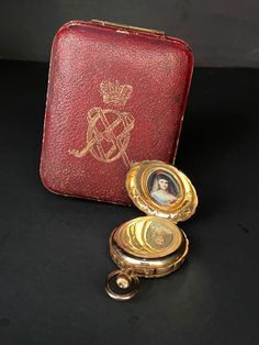 an antique pocket watch with a red leather case and gold - plated key chain