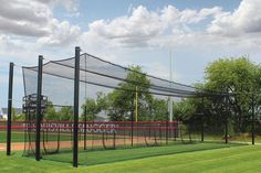 a baseball field with batting cages and trees in the background