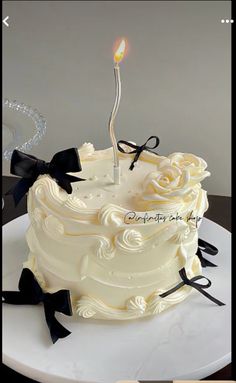 a white cake with black ribbon and a single candle sticking out of the icing