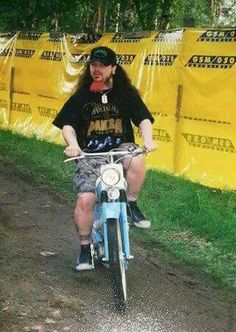 a man riding on the back of a blue bike down a dirt road next to a yellow sign