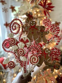 a person holding up some candy canes in front of a christmas tree with decorations