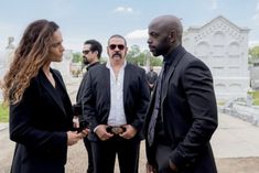 two men and a woman standing in front of a cemetery with one man looking at the other