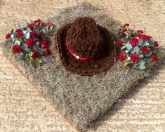 a brown hat with red flowers on it sitting on top of a pile of hay