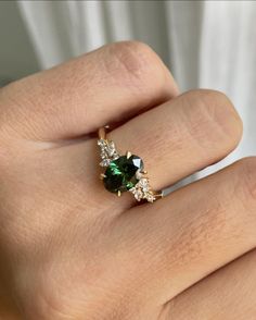 a woman's hand with a green and white diamond ring on her left hand