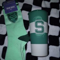 the socks are green and white on the bed next to the coffee cup that is sitting on top of it