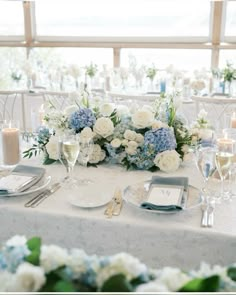 the table is set with blue and white flowers, silverware, candles, and napkins