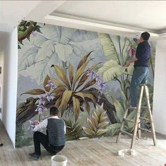 two men are painting a mural on the wall in a room with wooden floors and ladders