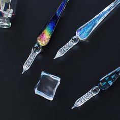 three different types of knifes on a black surface with some glass blocks and scissors in the foreground