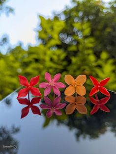 three paper flowers sitting on top of a black table next to green leaves and trees