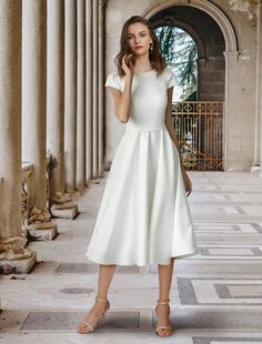 a woman wearing a white dress standing in an old building with pillars and columns on either side