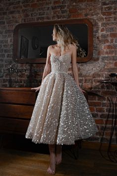 a woman standing in front of a brick wall wearing a dress with sequins