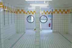 an empty public bathroom with yellow and white tiles on the walls, two round windows