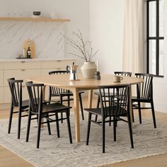 a dining room table with chairs and a vase on top of it in front of a window