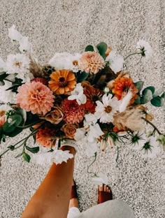 a person holding a bouquet of flowers in their hand on the ground with sand and gravel