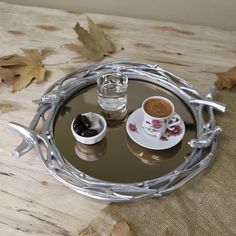 two cups and saucers sitting on a tray with leaves around the edge, next to each other