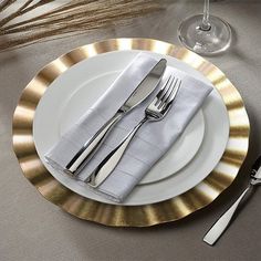 a table setting with silverware and gold rimmed placemats, forks and knives