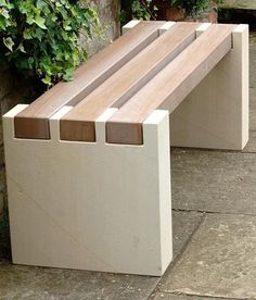 a wooden bench sitting on top of a cement slab next to a planter filled with green plants