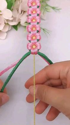 two hands are holding a piece of string with pink flowers on it and green stems