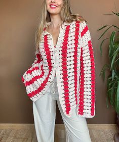 a woman standing in front of a wall wearing a red and white crochet jacket