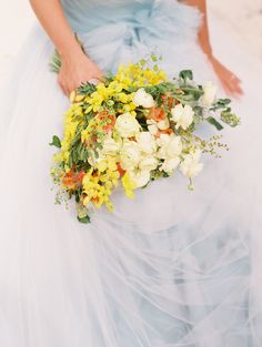 a woman in a blue dress holding a bouquet of yellow and white flowers on her wedding day