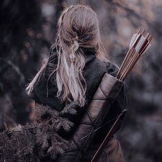 a woman with long hair holding two arrows in her hand and looking at the woods