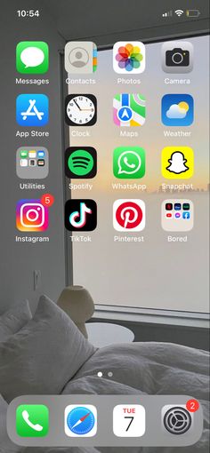 an iphone with icons on the screen and in front of a window that is open