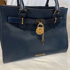 Beautiful Navy Bag With Gold Accents In Hardware Outside. Inside Is A Zippered Pocket On One Side And An Open Pocket On The Other. An Additional Adjustable Long Strap To Carry Over The Shoulder Comes With It. The Strap Clips On And Off Easily And Has The Gold Hardware. Bag Is 13” Across.Side To Side, Bottom Side Gusset Is 7”, Top To Bottom Or Depth Is 10”. The Gold Lock On Front Has A Key That Unlocks It And Can Release The Top Portion Of The Bag To Open Top Wider Creating A Box-Like Look. I Hav Blue Leather Bag With Lock, Blue Formal Bag With Turn-lock Closure, Luxury Navy Bags With Gold-tone Hardware, Blue Office Bag With Turn-lock Closure, Blue Travel Bag With Turn-lock Closure, Blue Everyday Bag With Lock, Blue Bags With Lock For Formal Occasions, Blue Leather Bag With Turn-lock Closure, Luxury Navy Shoulder Bag With Gold-tone Hardware