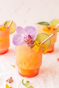 two cocktails with flowers and lime garnish on the rim, sitting on ice