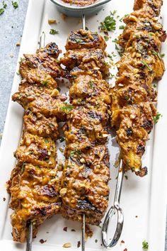 grilled chicken skewers on a white platter with a bowl of salsa