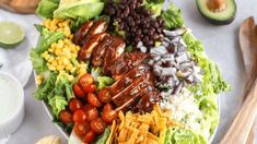 a large salad with dressing on top of it and other foods in the bowl next to it