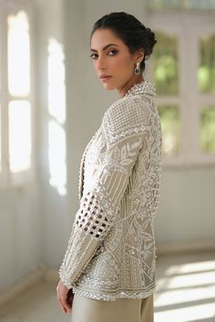 A slate coloured tissue jacket with folded lapels is rendered with intricate cutwork and thread and embroidery. Paired with ivory choli and slate-coloured charmeuse box trousers with embroidered hems; this outfit exudes sheer elegance. Model Height is 5'6 jacket length is 26" Indian Suit With Jacket, Elegant White Bandhgala With Mirror Work, Elegant Silk Nehru Jacket With Chikankari Embroidery, Elegant Silk Sherwani With Resham Embroidery, Elegant Long Sleeve Bandhgala With Resham Embroidery, Silk Bandhgala With Chikankari Embroidery For Wedding, Elegant Silk Bandhgala With Chikankari Embroidery, Elegant Nehru Jacket With Mirror Work For Festive Occasions, Wedding Silk Bandhgala With Chikankari Embroidery